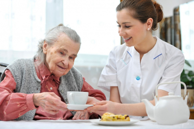 smiling caregiver giving a cup of tea or coffee to her old woman patient